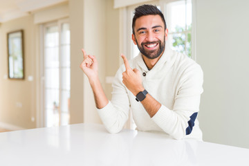 Fototapeta premium Handsome hispanic man wearing casual white sweater at home smiling and looking at the camera pointing with two hands and fingers to the side.
