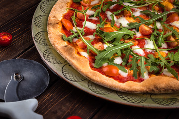 Closeup Pizza Margherita with Buffalo mozzarella, tomatoes and fresh basil. Pizza cutter lies on the wooden background. Traditional italian fast food