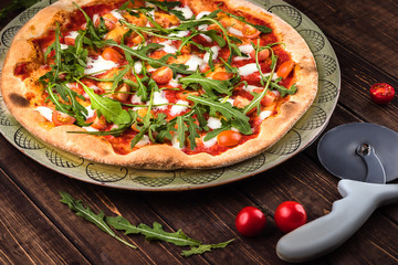 Closeup Pizza Margherita with Buffalo mozzarella, tomatoes and fresh basil. Pizza cutter lies on the wooden background. Traditional italian fast food
