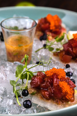 Closeup Red tuna tartare in ice on the green plate with lime and blueberries. Wooden brown background