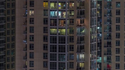 Fototapeta na wymiar Windows of the multi-storey building with lighting inside and moving people in apartments timelapse.