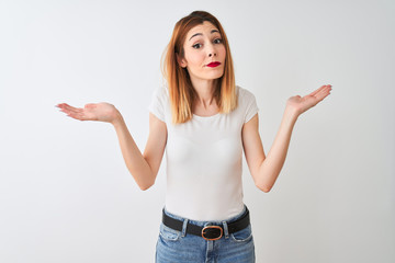 Fototapeta na wymiar Beautiful redhead woman wearing casual t-shirt standing over isolated white background clueless and confused expression with arms and hands raised. Doubt concept.