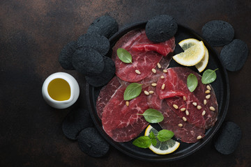 Carpaccio made of raw marbled beef and served with black potato chips, flatlay on a dark brown...