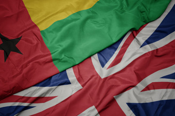 waving colorful flag of great britain and national flag of guinea bissau.