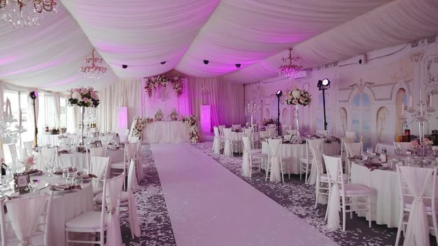 elegant banquet hall decorated in white style for wedding ceremony and lit with pink light in comfortable restaurant