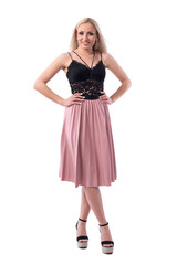 Cute pretty blonde woman in black lace top and salmon color skirt posing with arms on hips. Full body isolated on white background. 