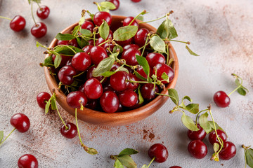 Fresh sweet cherries bowl with leaves on stone background, top view