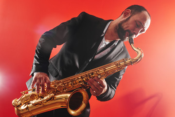 Portrait of professional musician saxophonist man in  suit plays jazz music on saxophone, red...