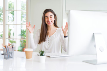 Beautiful young woman working using computer celebrating mad and crazy for success with arms raised and closed eyes screaming excited. Winner concept