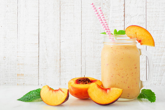 Peach smoothie in a mason jar glass with scattered fruit.  Side view with a white wood background.