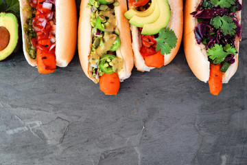 Carrot vegan hot dogs with assorted toppings. Above view top border on a slate background. Plant...