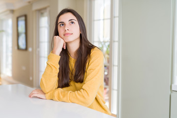 Fototapeta premium Beautiful young woman wearing yellow sweater with hand on chin thinking about question, pensive expression. Smiling with thoughtful face. Doubt concept.