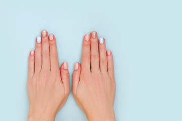 Woman's hands with pastel manicure on blue background with copy space.