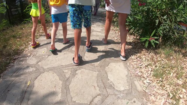 A short-legged baby is walking with friends.  A boy with foot disease in special shoes is walking along the road with friends.