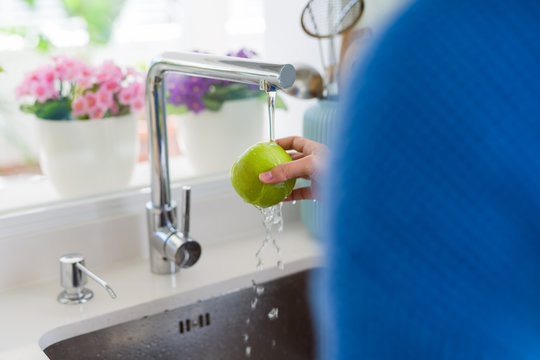 Young woman washing vegetables and fruit using water from sink