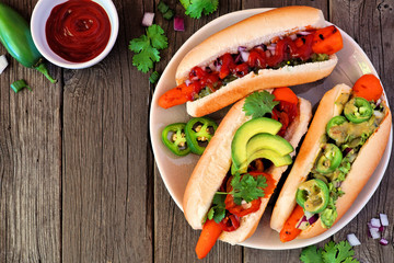 Carrot hot dogs with assorted toppings. Top view table scene with a rustic wood background. Plant...