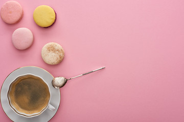 top view of delicious French macaroons near coffee with spoon on pink background with copy space