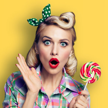 Photo of beautiful surprised woman with lollipop, dressed in pin-up style, yellow color background, square composition