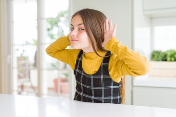 Young beautiful blonde kid girl wearing casual yellow sweater at home Trying to hear both hands on ear gesture, curious for gossip. Hearing problem, deaf