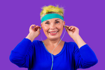 happy old cheerful female and a blue bandage on forehead,showing rocker grimace tongue and listen rock song on headphones.forever young soul