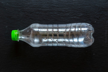 Empty plastic bottle placed horizontally on a black background – Drinking recipient with green cap on a stone textured surface – Concept image for recycling and pollution