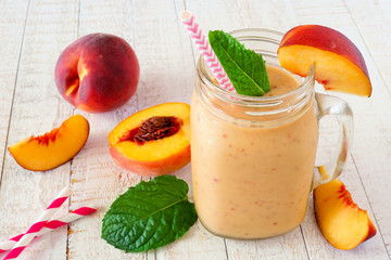 Healthy  peach smoothie in a mason jar glass. Close up table scene against a white wood background.