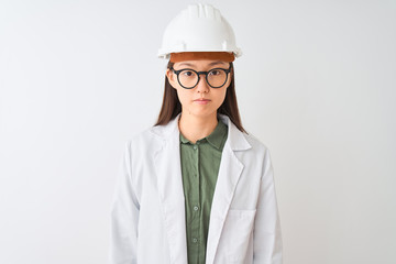 Young chinese engineer woman wearing coat helmet glasses over isolated white background Relaxed with serious expression on face. Simple and natural looking at the camera.