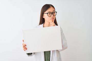 Young chinese dooctor woman wearing glasses holding banner over isolated white background serious...