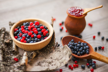 Blueberry and raspberry berry jam in a clay pot, a wooden spoon with fresh berries and birch bark...