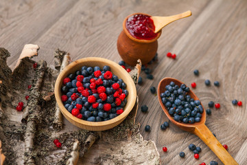 Blueberry and raspberry berry jam in a clay pot, a wooden spoon with fresh berries and birch bark on a wooden background