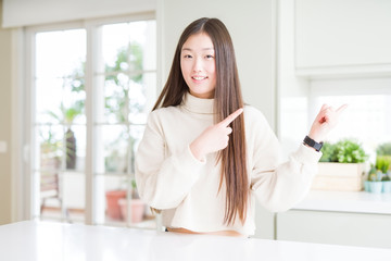 Beautiful Asian woman wearing casual sweater smiling and looking at the camera pointing with two hands and fingers to the side.