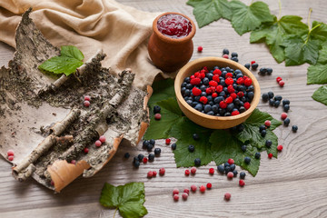 Blueberry and raspberry berry jam in a clay pot with fresh berries, birch bark and a linen...