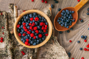 Blueberry and raspberry berry jam in a clay pot, a wooden spoon with fresh berries and birch bark on a wooden background