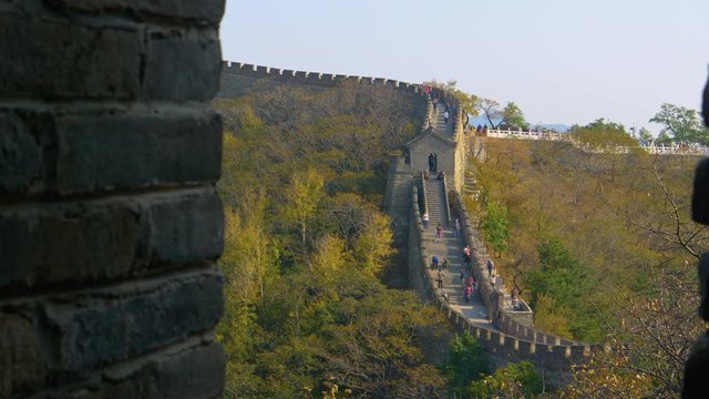 CLOSE UP: Stone wall creates a window offering a view of tourists exploring the Great Wall of China and the surrounding forest covered mountains. Cinematic shot of travelers walking up an ancient wall