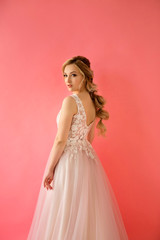 portrait of a beautiful young woman with makeup and hairstyle in a beautiful dress on a pink background