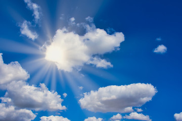 Naklejka na ściany i meble sun is shining bright through white clouds on a blue sky, with sun rays