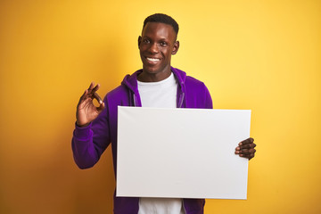African american man holding banner standing over isolated yellow background doing ok sign with fingers, excellent symbol