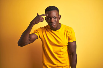 Fototapeta na wymiar Young african american man wearing casual t-shirt standing over isolated yellow background pointing unhappy to pimple on forehead, ugly infection of blackhead. Acne and skin problem