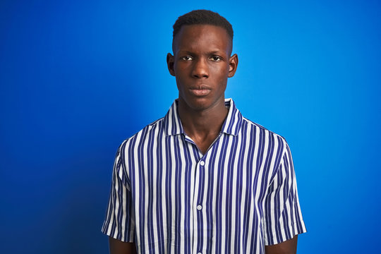 African american man wearing striped casual shirt standing over isolated blue background with serious expression on face. Simple and natural looking at the camera.