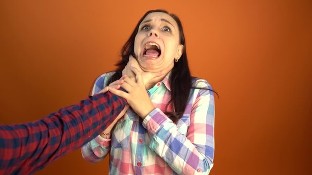 A man's hand in a shirt strangles a scared young woman on an orange background. The concept of stop domestic violence against women.
