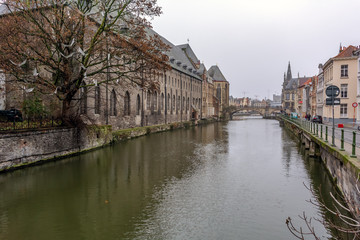 Fototapeta na wymiar Old street of morning Ghent, Belgium, with traditional medieval houses, canal, bridge, tower in the background and white paper birds on the tree in the foreground.
