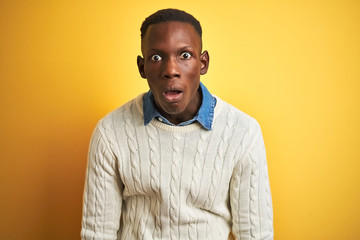 Fototapeta premium African american man wearing denim shirt and white sweater over isolated yellow background afraid and shocked with surprise and amazed expression, fear and excited face.
