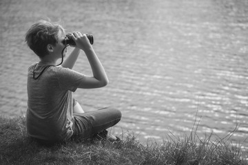 Black and white photography of cute happy kid wathing in old vintage binocular at something interesting in distance.
