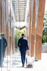 back view of businessman in suit with hand in pocket holding suitcase