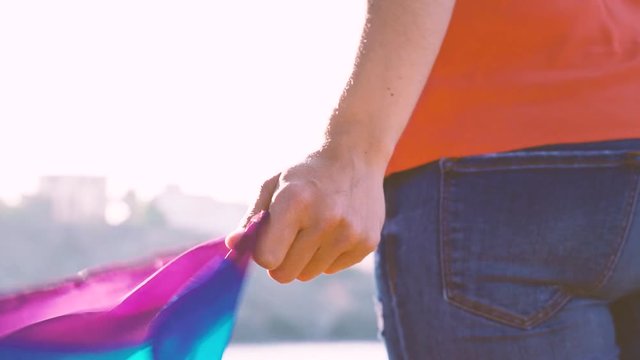 Close up of a woman hand holding a pride flag. The wind blow the lgbt colors with proud and equality. New generation free of prejudices. Free choice of sexual orientation for young people. 