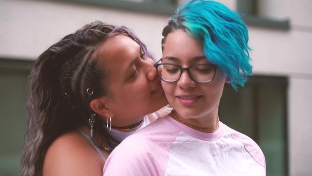 Modern cool young lesbian girlfriends in love. Woman kissing her fiance neck in public. Lesbian teen couple kissing in a public place. Not embarrassed of their sexuality. Proud to be gay. 
