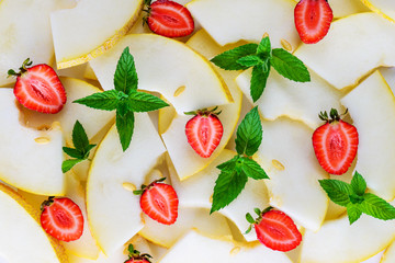 Melon slices, strawberry and mint leaves as background. Flat lay, closeup.