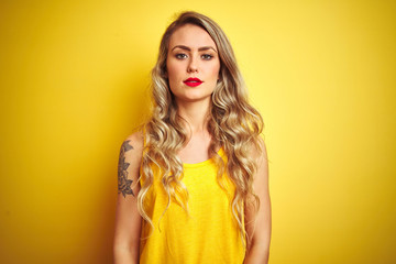 Young beautiful woman wearing t-shirt standing over yellow isolated background with serious expression on face. Simple and natural looking at the camera.