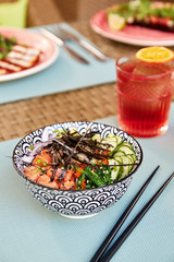 Bowl of asian soup miso with raw salmon, seaweeds, avocado, cucumber, onion, sea vegetables, flying fish roe, sesame and ginger in bowl on table in street cafe