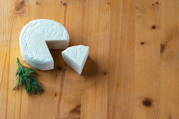Homemade cheese wheel and dill on wooden board